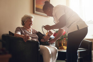 Nurse measuring blood pressure of senior woman patient in retirement home. Home caregiver doing routine checkup of a mature female patient.