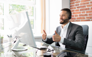 Customer service agent bearded man on video call with client, giving two thumbs up to camera. Business man is smiling and wearing a headset. VOIP connection.