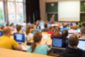 blurred classroom with laptops and teacher at front