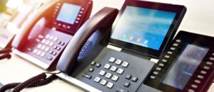 Array of PBX VOIP phone systems in a row that are turned on and working. Natural sunlight coming in from left of image to illuminate room.