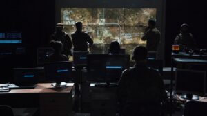 group of people viewing monitors with large overhead display