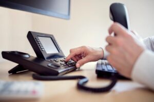 Person holding phone in one hand and pressing key on pbx voip phone system using other hand and reaching over keyboard.