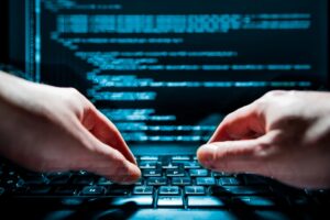 hands typing onto laptop keyboard with code on monitor of screen