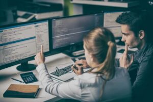 blonde woman helping man at computer pointing to HTML code